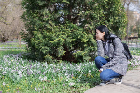 Portrait of young brunette woman in a plaid coat in park and looking away enjoying the nature in beautiful spring dayの写真素材