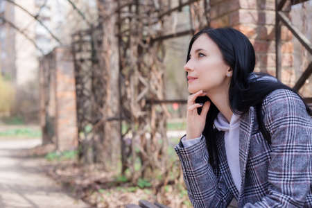 Portrait of young brunette woman in a plaid coat in park and looking away enjoying the nature in beautiful spring dayの写真素材