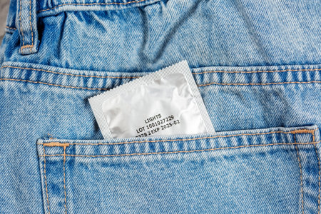 Close-up of a pocket of blue jeans from which a condom sticks out, safe sex conceptの写真素材