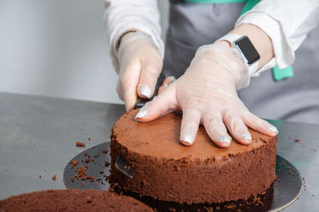 Womans hands chef cutting chocolate cake layers and stacking them on metal table. Making Chocolate Layer Cake. Series.の写真素材