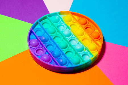 Top view of the sensory toy pop it on the multicolored background.Rainbow color.Antistress toy for...