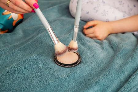 Woman hands of mom and daughter gaining compact powder on a large fluffy cosmetic brush. Close-up...