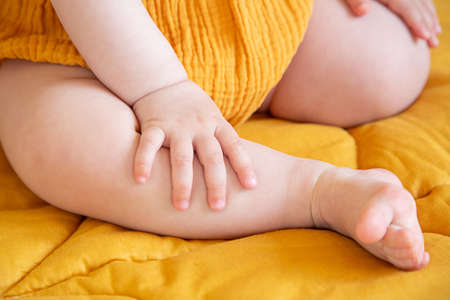 Hands and feet of a child in yellow clothes on a yellow blanket.の写真素材