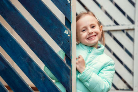 Little caucasian blonde girl in fashionable clothes posing with smile looking at the camera from...