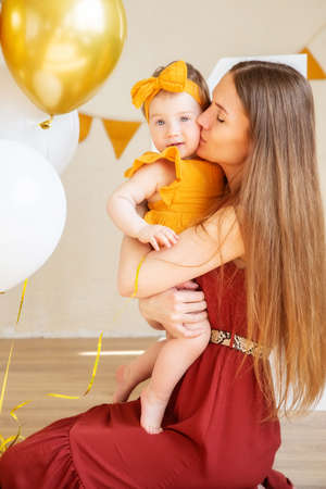 Happy mom kisses her one-year-old daughter in yellow clothes, studio photo for a year of the childの写真素材