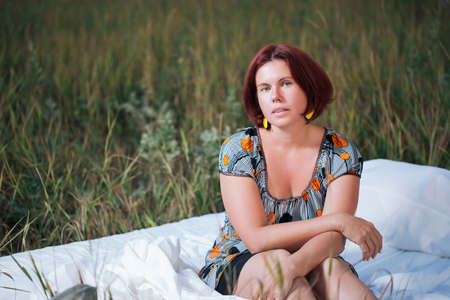 Charming caucasian woman 30-35 years old in the white bed in a field at sunset in summer looking at...