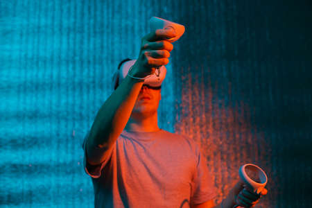 Young caucasian man 25-30 years using virtual reality headset. VR, future, gadgets, technology concept in neon light.の写真素材