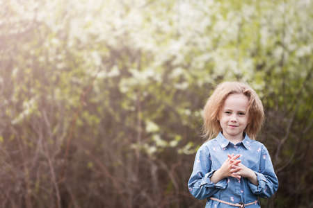 Portrait of adorable little caucasian girl 5 years old in the park standing under the cherry blossoms with selective focus and blurred backgroundの写真素材