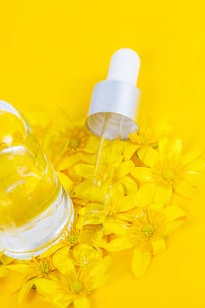 A bottle with a pipette serum on a yellow background surrounded by spring flowersの写真素材