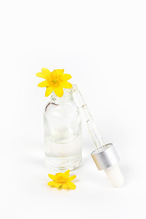 A bottle with a pipette serum on a white background surrounded by yellow spring flowersの写真素材