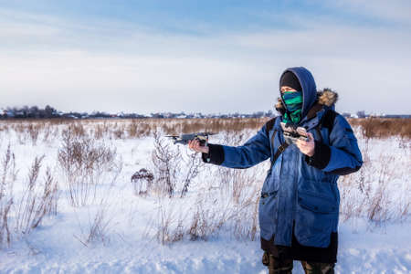 Caucasian Male in the blue jacket launching a flying drone with a remote controller in his hand on winter field.の写真素材