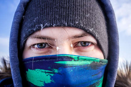 Close up view of a caucasian man face with scarf and hooded winter jacket with frost on the eyebrows...