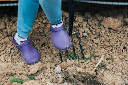 The girl digs the soil with a pitchfork in the garden to prepare a hole for planting a plant
