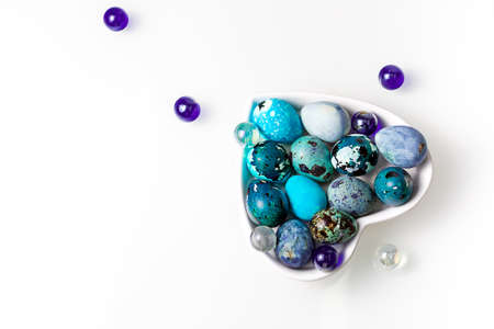 Easter blue quail eggs in a plate in the shape of a heart on a white table.の写真素材