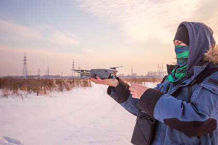 Caucasian Male in the blue jacket launching a flying drone with a remote controller in his hand on winter field.の写真素材