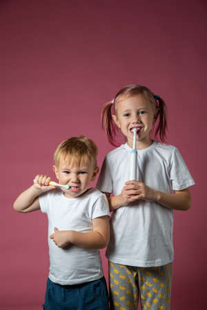 Smiling caucasian little boy and girl cleaning his teeth with electric sonic and manual toothbrush on pink background.の写真素材