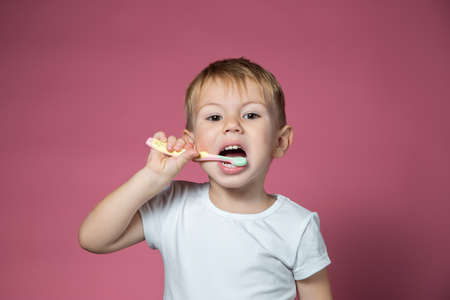 Smiling caucasian little boy cleaning his teeth with manual children toothbrush on pink background.の写真素材