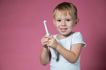 Smiling caucasian little boy holds electric sonic toothbrush on pink background.の写真素材