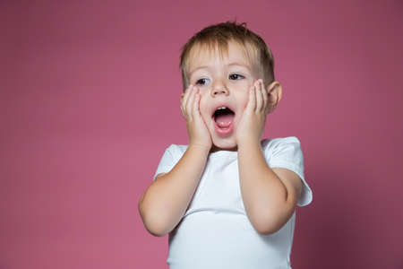 Caucasian boy 3 years old makes scary faces while looking at the camera on a pink backgroundの写真素材
