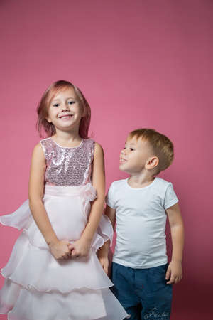 Caucasian brother and sister, hugging on camera on pink background studio shot. Family ties, friendship, happy childhood concept.の写真素材