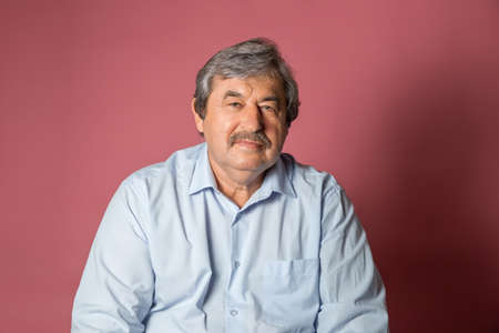 Portrait of elderly man on pink color background looking at cameraの写真素材