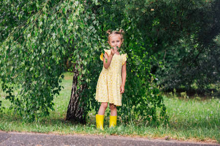 Portrait of caucasian girl of 6 years in yellow dress and rainboots standing in the parkの写真素材