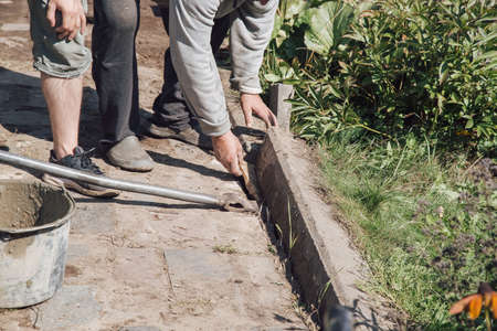 Men lay curbstone for grouting garden path, construction work on garden plotの写真素材