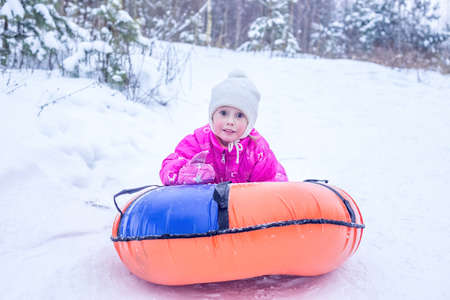 A cheerful girl in warm clothes rides down snowy hill on slide-slide cheesecake