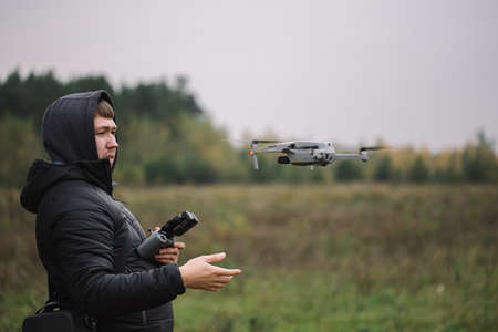 Man holding drone and remote control against field background.