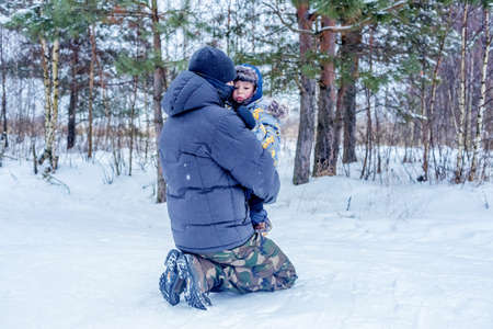 Dad holds and hugs his little son in a snowy forest or winter park. Concept of winter outdoors activities for family.の写真素材