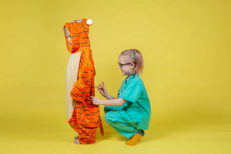 Little caucasian Children play doctor, a girl dressed as a doctor gives an injection to a boy...