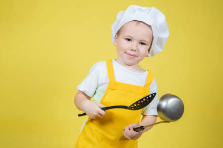 Little caucasian Boy playing chef, boy in apron and chef's hat posing on yellow backgroundの写真素材