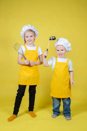 Children playing chefs, boy and girl in an apron and a chef's cap are posing on a yellow backgroundの写真素材