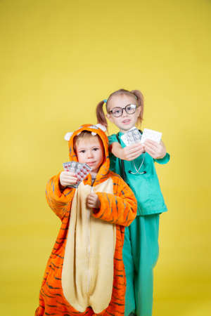 Children play doctor, a girl dressed as a doctor and a boy dressed as a tiger hold blisters with pills in their handsの写真素材
