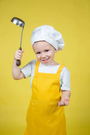 Little caucasian Boy playing chef, boy in apron and chef's hat emotionally posing on yellow backgroundの写真素材