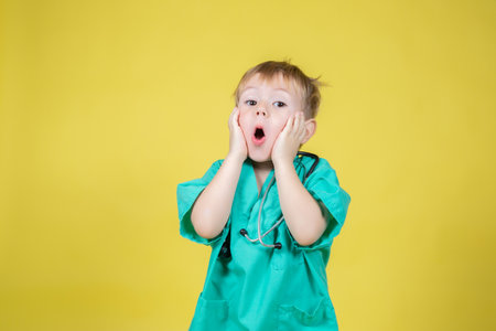 Portrait of shocked little caucasian boy dressed in doctors green posing emotionally on yellow backgroundの写真素材