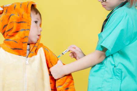 Little caucasian Children play doctor, a girl dressed as a doctor gives an injection to a boy dressed as a tigerの写真素材