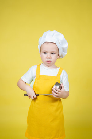 Little caucasian Boy playing chef, boy in apron and chef's hat emotionally posing on yellow backgroundの写真素材