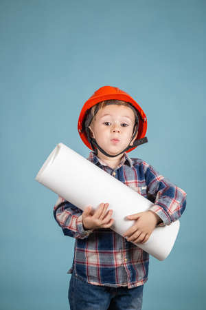 Portrait of cute little caucasian child builder in hardhats holding construction drawing against...
