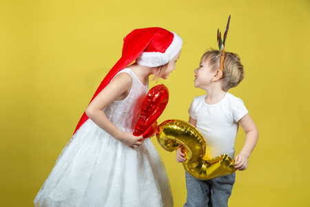 Adorable caucasian kids in christmas Santa hat and reindeer costume holding balloons with numbers...