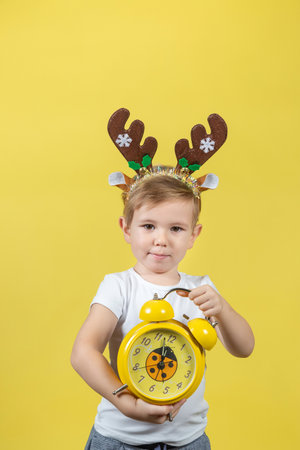 A smiling little boy in christmas reindeer costume with alarm clock in his hands. A place for your...