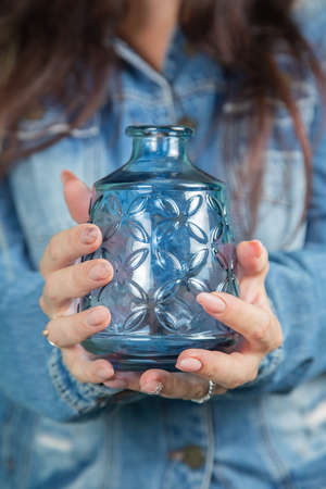 Female hands hold an empty glass vase of blue glass.の写真素材