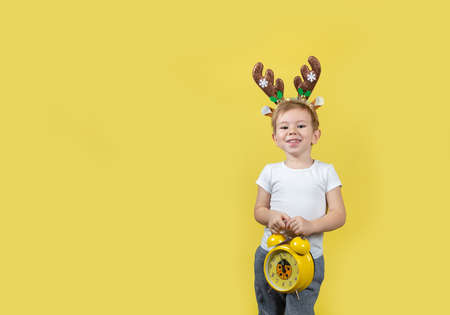 Cute caucasian boy in in christmas reindeer costume with alarm clocks in his hands making funny...