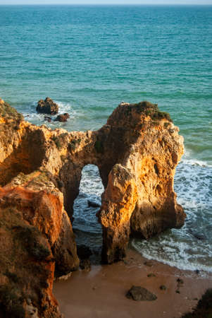 Orange-colored rocks form an arch at the beachの写真素材
