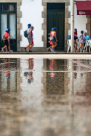 Children passing by in the reflection of wet pavement, Portuguese street - Vertical.