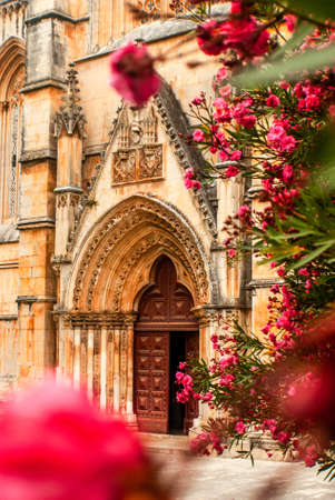 Gothic entrance of the Monastery of Batalha in pink blooming oleander flowers in the foreground - Nerium oleander, Batalha, Portugal, Vertical, Selective focusの写真素材