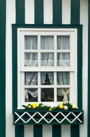 A window of a rural decorative country house in green and white stripes with yellow flowers on the...