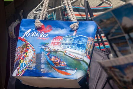Aveiro, Portugal - June 11, 2021: Souvenir colorful bag in the street shop with a landscape of Aveiro canal and a gondola colorful boat on it and postcards in the foreground, Text Aveiro city Portugalのeditorial素材