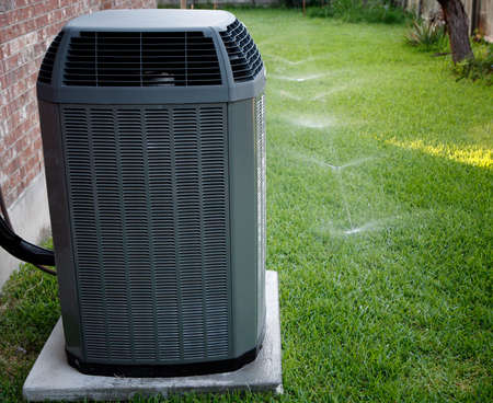 Modern air conditioner on backyard with working sprinkler system Modern air conditioner on backyard with working sprinkler system