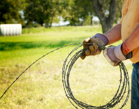 Fencing and safety: Man's hand working on barbed wire farm fence with blood cut.の写真素材
